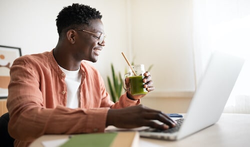 Photo d'un homme souriant devant son ordinateur de travail et buvant un smoothie sain.