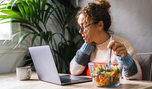Photo d'une femme devant son ordinateur en train de manger une salade.